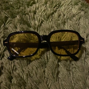 Svarta glasögon med gula linser - Ett par snygga retroinspirerade glasögon med svart, fyrkantig båge och gula linser. Perfekt för dig som vill sticka ut med en cool och unik look. Bågarna har en klassisk form som passar till många stilar.