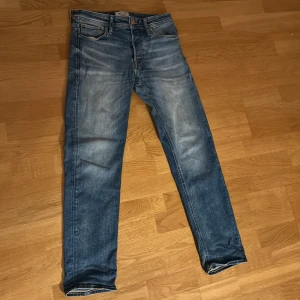Blå jeans från Jack & Jones - Snygga blå jeans från Jack & Jones med klassisk femficksdesign och slitna detaljer. Jeansen har en smal passform och är tillverkade i mjukt denimtyg som ger en bekväm känsla. Perfekta för dig som gillar en stilren och avslappnad look. Storlek 28x30
