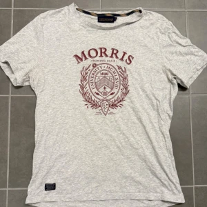 Grå t-shirt Morris - Snygg ljusgrå t-shirt från Morris Rowing Club med klassiskt universitetsinspirerat tryck i vinrött på bröstet. Rund hals och korta ärmar, perfekt för en chill och sportig look. Mjuk bomullskvalitet som känns skön mot huden. Storlek M
