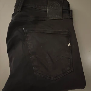Svarta Replay Anbass Hyperflex jeans - Svarta Replay Anbass Hyperflex jeans med klassisk femficksdesign och snygga detaljer som Replay-logga på fickan och bakre läderpatch. Slimmad passform och stretchigt material för extra komfort. Perfekt för dig som gillar stilrena och moderna jeans. Rätt trött skick och lite missfärgning som jag tror blivit av solen, dem har även några fläckar på insidan av dem som inte går att se så mycket men man känner att de är lite hårt där, förvinner nog med kemtvätt. W30 (40cm) och 102cm långa. 