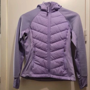 Ljuslila pufferjacka från H&M Move - Snygg ljuslila pufferjacka från H&M Move med huva och hel dragkedja framtill. Jackan har quiltad design på bröst och rygg, samt ribbade detaljer på ärmar och axlar. Två fickor med dragkedja på sidorna. Perfekt för kyliga dagar.