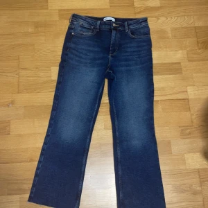 Blå raka jeans från Zara helt oanvända - Snygga blå jeans från Zara med klassisk femficksdesign och raka ben. Jeansen har en mörk tvätt med lätt slitning framtill, normal passform och hög midja. Materialet är robust denim med bruna sömmar och läderpatch med Zara-logga bak.