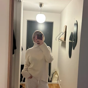 Vit polotröja i kashmir från Davida - Supermjuk och lyxig vit polotröja från Davida i kashmir. Tröjan har en hög, ribbad polokrage och långa ärmar med breda muddar. Passformen är loose och den är perfekt för att hålla sig varm under kyliga dagar. Stilren och enkel design som är lätt att matcha. Nypris 3000 kr.