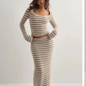 Nelly randig stickat set - Supersnygg långkjol från Nelly med stickat material i beige och vitt. Kjolen har ett randigt mönster och sitter tajt längs kroppen. 