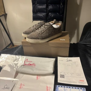 Gråa sneakers från Christian Louboutin - Snygga gråa sneakers från Christian Louboutin i mocka med rund tå och platt sula. Skorna har klassisk snörning och en stilren design som passar till många olika outfits. Kommer med originalkartong, dustbag och kvitto.