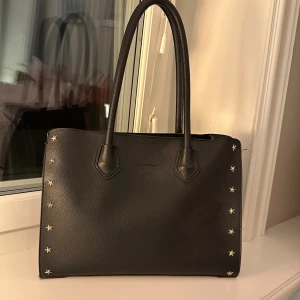 Skolväska - Superfin svart väska med sjärnor på kanterna. Passar perfekt till skolan då dator och skolböcker får plats. Man ser ungefär hur stor det är på andra bilden men annars står mått.