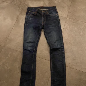 Mörkblå Nudie Jeans - Snygga mörkblå jeans från Nudie Jeans med klassiska orange sömmar och broderad bakficka.      W 30 L 32