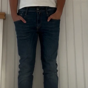 Blå slim fit jeans från Replay - Säljer ett par blå slim fit jeans från Replay med klassisk femficksdesign och snygga detaljer på bakfickorna. Jeansen har normal midja och är tillverkade i stretchigt denim för en bekväm passform. Perfekta för dig som gillar en modern och stilren look. Storlek 31:32
