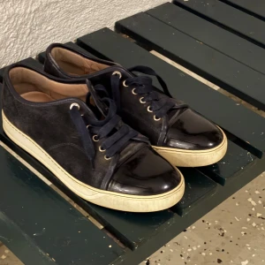 Lanvin marinblå  sneakers i mocka och lack -  Säljer nu mina lanvin skor som blivit för små!Snygga marinblå  sneakers från Lanvin med ovandel i mocka och lackad tå. Skorna har vita gummisulor, marinblå skosnören och metallfärgade öljetter. Klassisk och stilren design som passar till det mesta. Perfekta för dig som gillar lyxiga detaljer och premiumkänsla. Skulle säga 7/10 i condition. Kan tänka mig gå ner i pris vid smidig affär. 