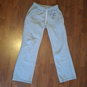 Grå mjukisbyxor med snörning - Grå mjukisbyxor från Equip med broderad logga och fjärilar på ena höften. Byxorna har resår i midjan med vit snörning och raka ben. Perfekta för chill eller träning, superbekväma och lätta att matcha med hoodies eller t-shirts.