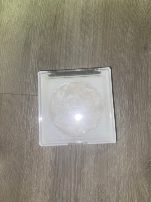Vit highlighter med diamantmönster - Säljer en skimrande vit highlighter i en fyrkantig vit plastförpackning med genomskinligt lock. Pudret har ett snyggt diamantmönster och innehåller mica för extra glow. Perfekt för att ge ansiktet en fräsch och glittrig finish.