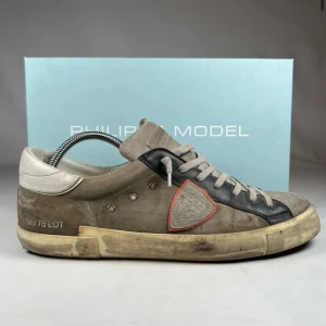 Philippe Model grå sneakers mocka - Snygga sneakers från Philippe Model i grå och svart mocka med beige detaljer och snörning. Skorna har en rund tå, platt sula och en unik sköldpatch med röd kant på sidan. Vit häl och slitna vintage-vibbar ger en cool streetstil. Kommer med skoboxen