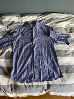 Blåvit rutig skjorta från Bläck - Snygg blåvit rutig skjorta från Bläck med regular fit och easy iron-material. Skjortan har klassisk krage, långa ärmar med manschett och vita knappar framtill. Perfekt för dig som gillar stilrena detaljer och bekväma plagg.