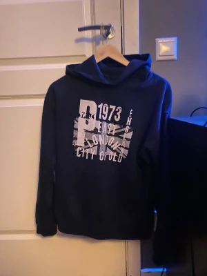 Mörkblå hoodie med tryck. - Säljer en mörkblå hoodie med tryck, storlek M. passar nån som är 170-180.