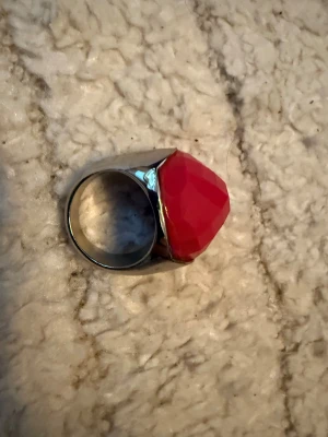 Stor silverring med rosa sten - Säljer en chunky silverfärgad ring med en stor, multifacetterad rosa sten på toppen. Ringen har en bred och stabil design som verkligen sticker ut. Perfekt för dig som gillar att göra ett statement med dina accessoarer.