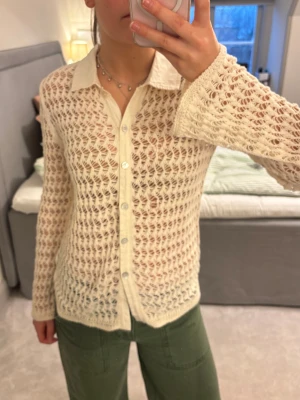 Virkad skjorta - En krämvit skjorta med lång ärm och virkat mönster. Skjortan har krage och knäppning framtill med pärlemorknappar. Materialet är stickat och passformen är normal.