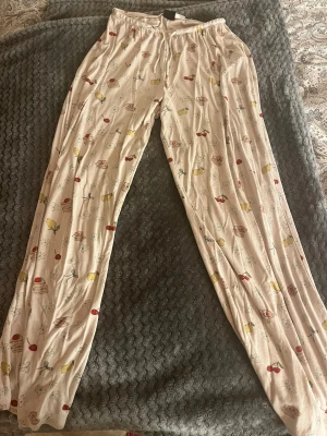 Beige mjukisbyxor med sött mönster - Supermysiga beige mjukisbyxor i storlek xs med elastisk midja och snörning. Byxorna har ett gulligt mönster med körsbär, citroner, blommor, tårtbitar och små koppar i rött, gult och blått. Perfekta för chill dagar hemma eller som pyjamasbyxor. Jag säljer dom för att jag köpte dom i en förliten storlek. Så dom är bara använda fåtal gånger!! 🥰🥰