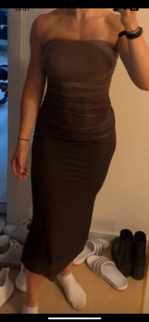 Brun axelbandslös långklänning - Säljer en snygg brun axelbandslös långklänning med figurnära passform. Klänningen har en enkel och stilren design utan mönster och är perfekt för dig som gillar minimalistisk stil. Materialet är stretchigt och sitter tight mot kroppen.