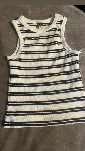 Randig ribbad linnetopp från Pieces - Säljer en vit och svart randig linnetopp från Pieces.Toppen är ribbad och ärmlös med rund halsringning. 