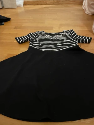 Randig paljettklänning Holly & Whyte - Svart och vit kortklänning från Holly & Whyte med randig överdel, paljettdetaljer på bröstet och halvlånga ärmar. Kjolen är helsvart och har en lätt utställd form. Perfekt för dig som gillar lite extra bling i vardagen.