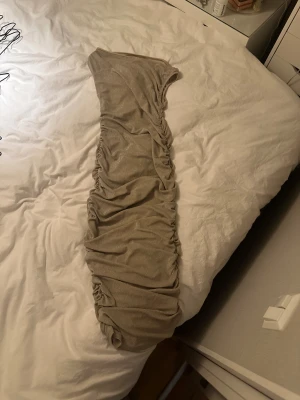 Glittrig beige långklänning - Säljer en snygg glittrig beige långklänning med rynkade detaljer längs sidorna. Klänningen har en figurnära passform och är ärmlös, perfekt för dig som vill sticka ut med en elegant look. Materialet är mjukt och skimrar snyggt i ljuset.