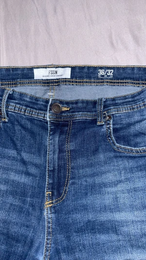 FSBN blå jeans straight fit 36/32 - Blå jeans från FSBN i klassisk straight fit med fem fickor och snygga kontrastsömmar. Jeansen har normal passform och är tillverkade i slitstarkt denimtyg. Perfekt för dig som gillar enkel och stilren look.