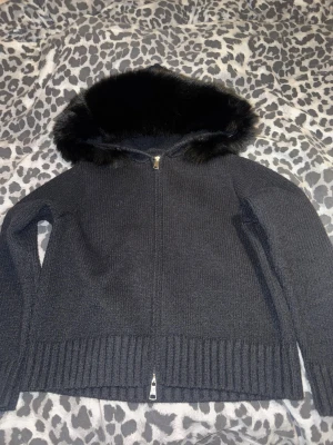 Alessa jacka - Mysig svart stickad jacka från Alessa med fluffig päls på huvan. Jackan har ribbade muddar, dragkedja framtill och långärmade ärmar. Aldrig använd.