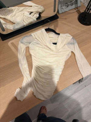 Krämvit långärmad omlottklänning - Supersnygg krämvit klänning med långa ärmar och omlott-detalj vid halsen. Klänningen har draperad effekt över hela kroppen och är figurnära. Perfekt för dig som gillar stilrena och eleganta plagg med en twist.