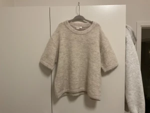 Beige stickad tröja Gina Tricot - Mysig beige stickad tröja från Gina Tricot med grov ribbad rund halsringning och halvkort ärm. Tröjan har en loose passform och är perfekt för lager-på-lager under hösten och vintern. Enkel och stilren.