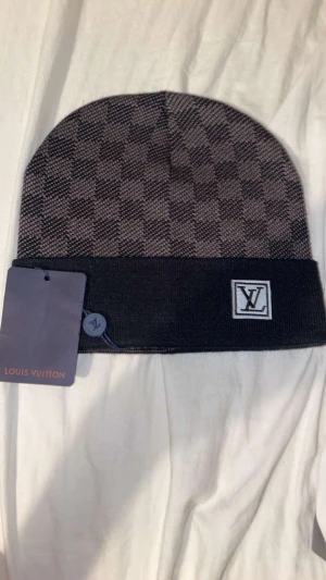 Svart mössa - Snygg svart och grå mössa med klassiskt rutigt mönster. Mössan är stickad och har en vikt kant. Perfekt accessoar för att lyfta din vinterstil.