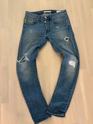  Tramarossa 2020 jeans - Snygga blå jeans från Tramarossa med coola slitningar och hål på benen. Modellen har raka ben, klassisk femficksdesign och detaljer med '2020' på ficka och bak. Jeansen är tillverkade i jeansmaterial och har en modern, streetig vibe.