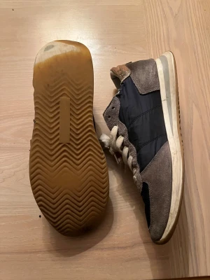 Philippe Model sneakers i svart och beige - Snygga sneakers från Philippe Model med svart textil och beige mockadetaljer. Skorna har rund tå, platt sula och vita snören. Insidan är fodrad med ljus skinn. Slitna under annars är sicket helt okej. 