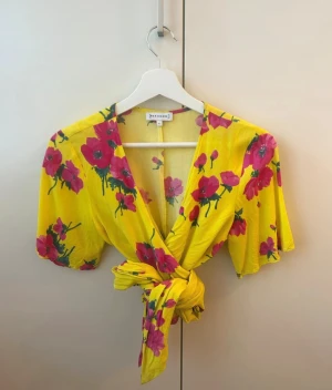 Warehouse Gul blommig omslagsblus Żółtakwiecista bluzka kopertowa - Gul omslagsblus med rosa blommönster från WAREHOUSE. Knyts i midjan. Kort ärm. Använd vid två tillfällen , mycket bra skick.