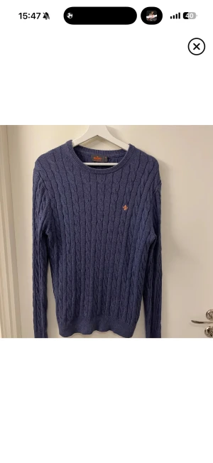 Blå kabelstickad tröja från Morris - Säljer en blå kabelstickad tröja från Morris i 100% pima bomull. Tröjan har rund halsringning, lång ärm och en broderad orange logga på bröstet. Perfekt för dig som gillar klassisk och stilren look. Skick 9/10 nypris cirka 1299