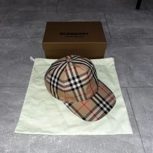 Burberry keps    - Snygg keps från Burberry med det ikoniska rutiga mönstret. Justerbar baktill med svart spänne och Burberry London England-logga. Säljer den pga att de inte är min stil, har använt den ett par gånger men den är fortfarande i topp skick.