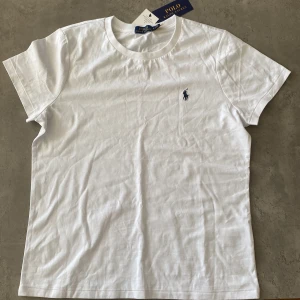 Vit Polo t-shirt - Klassisk vit t-shirt från Polo Ralph Lauren med rund hals och korta ärmar. T-shirten har en liten broderad logga i marinblått på bröstet och är gjord i mjuk bomull. Perfekt basic-plagg med snygg passform och stilren look.