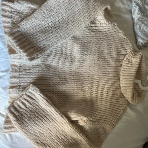 Beige stickad polotröja - Mysig och chunky beige stickad polotröja med breda ribbade muddar och hög krage. Perfekt för kyliga dagar. 