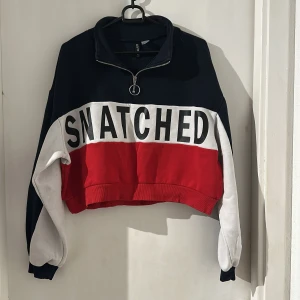 Colorblock croppad tröja med tryck - Trendig croppad tröja från Stradivarius med svart, vit och röd colorblock-design. Stort SNATCHED-tryck framtill, half zip med ringdetalj och långa ärmar. Perfekt för en cool streetstyle-look.