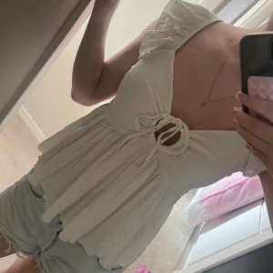 Vit omlottopp med volang och snörning - Supersöt vit topp med volangärmar och omlottkänsla framtill. Toppen har snygg snörning vid bysten och är tillverkad i ett lätt, luftigt tyg som ger en flowy siluett. Perfekt för varma dagar och ger en romantisk vibe.