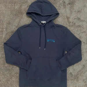 Mörkblå hoodie från Maison Kitsuné - Säljer en mörkblå hoodie från Maison Kitsuné i storlek S. Tröjan har huva med dragsko, känguruficka och diskret logga i blått på bröstet. Tillverkad i mjuk bomull och har en klassisk, normal passform. Perfekt för chill dagar eller när du vill vara bekväm.