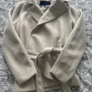 Beige kappa från Vero Moda med bälte - Snygg beige kappa från Vero Moda med klassisk krage och knytbälte i midjan. Den perfekta jackan nu till hösten. Säljs då den inte kommer till användning🧡