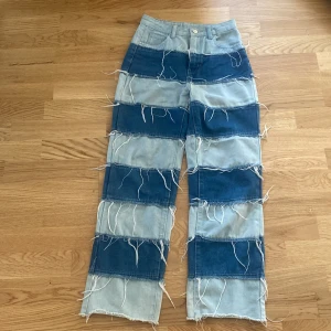 Patchade jeans i två denimfärger - Unika jeans med breda block i ljus och mörkblå denim, dekorerade med råa kanter och fransiga detaljer. Raka ben och klassisk femficksmodell. Perfekta för dig som vill sticka ut med en kreativ och edgy stil.