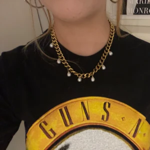 Chunky guldhalsband med pärlor rostfritt - Snyggt chunky halsband i guld med stora länkar och hängande vita pärlor. Kedjan har en cool och trendig vibe som passar perfekt till en statement-look. Pärlorna ger en extra touch av elegans till det robusta guldfärgade halsbandet.