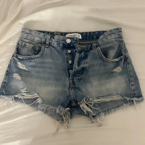 Blå jeansshorts  - Säljer ett par blå jeansshorts från Pull&Bear. Shortsen har slitna detaljer och knappar framtill, samt klassiska fickor både fram och bak. Perfekta för en chill sommarlook.