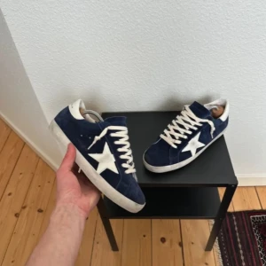 Blå mockasneakers med vit stjärna - Snygga sneakers i mörkblå mocka med vit stjärndetalj på sidan och vita snören. Skorna har en klassisk låg profil och vit sula, perfekt för dig som gillar streetstyle. Runda tår och platt sula ger en avslappnad vibe.
