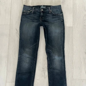 Blue Cult jeans med fickdetaljer - Supersnygga mörkblå jeans från Blue Cult med snyggt slitna detaljer och raka ben. Bakfickorna har dekorativa strass i guld och silver diamanter/pärlor. Klassisk femficksmodell med låg midja och cool broderad logga på insidan. Lite 2000-tals vibe🥰Jeansen är raka men går ganska nära benen. (sista bilden kan vara en fläck, men absolut inget man tänker på!)