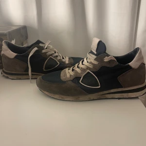 Philippe Model sneakers i mocka och textil - Snygga sneakers från Philippe Model i mörkblått och beige med detaljer i mocka och textil. Skorna har vita snören, rund tå och klassisk logga på sidan. Perfekta för dig som gillar en stilren men sportig look.