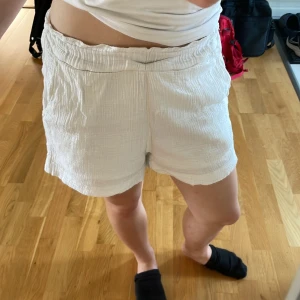 Vita bomullsshorts från Lindex XS - Säljer ett par vita, luftiga shorts från Lindex i storlek XS. De har hög midja med resår och är tillverkade i mjuk, krinklad bomull. Perfekta för varma sommardagar och har en avslappnad, loose passform.