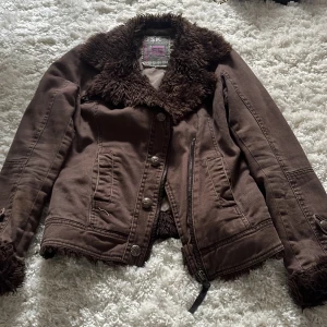 Brun teddyjacka från BSK med pälsdetaljer - Säljer en brun teddyjacka från BSK i storlek S. Jackan har fluffig pälsimitation vid krage och ärmslut, samt både knappar och dragkedja framtill. Snygga sömmar och två fickor på framsidan. Perfekt för dig som gillar coola detaljer och vill ha en unik look.