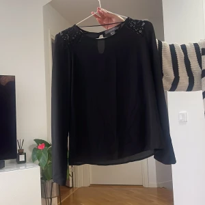 Svart blus med spetsdetaljer - Svart blus från H&M med långa ärmar och fina spetsdetaljer på axlarna. Rund halsringning med liten öppning framtill. Tunn och luftig modell som faller snyggt.